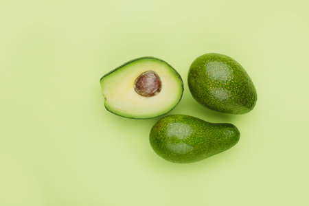 Two whole and half avocados on a green background, minimalistic top view