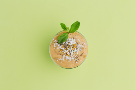 A glass of fruit smoothie with coconut shavings and chia seeds and a sprig of mint on green background, の写真素材