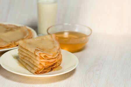 Maslenitsa is a holiday at the end of February . pancakes with honey and milk on a light background. honey trickles down a stack of pancakes. close up. blini. space for text.の写真素材