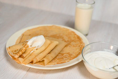 Maslenitsa is a holiday at the end of February . pancakes with sour cream and milk on a light wooden...