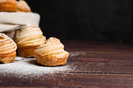 Delicious modern cruffins are made from layered croissants in the shape of a muffin. cruffins with a wooden basket on a dark background, sprinkled with powdered sugar. Copy space.の写真素材