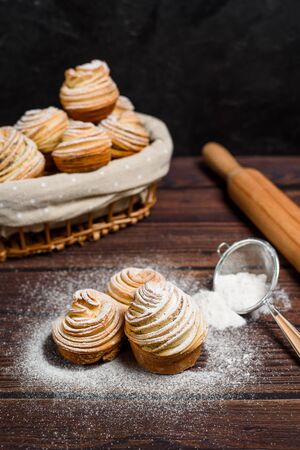 modern cruffins are made from puff croissants in the form of a muffin. in a wooden basket on a dark background, sprinkled with powdered sugar. Copy space. the view from the top..の写真素材