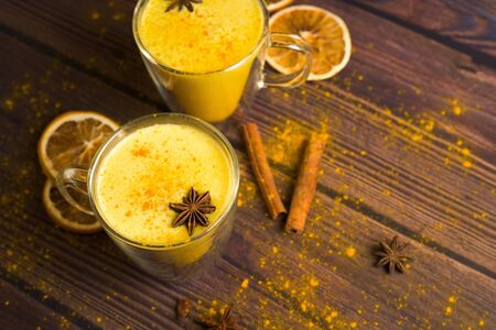 Golden milk drink with turmeric and honey on a dark wooden background in transparent glasses for health . spices dissolved in warm milk with honey and spices. place for text top view.の写真素材