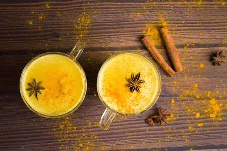 Golden milk drink with turmeric and honey on a dark wooden background in transparent glasses for health . spices dissolved in warm milk with honey and spices. place for text top view.の写真素材