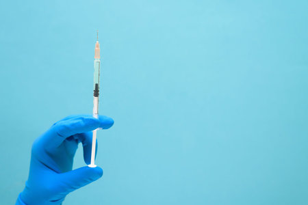 virus vaccine in hand in a medical blue glove against coronavirus on a blue background. space for...
