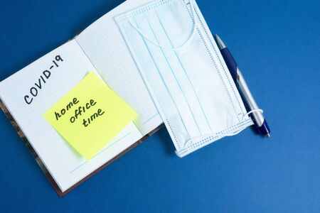 text-coronavirus, stay at home, office at home written on a Notepad by hand. the view from the top. Mask and ballpoint pen with Notepad on a blue background. the concept of pandemics, self-isolation.の写真素材