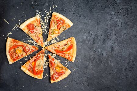 round fresh vegetarian pizza cut into pieces and sprinkled with cheese on a dark background.tomatoes, mushrooms, peppers, Basil and pizza cheese . space for text. the view from the top.の写真素材