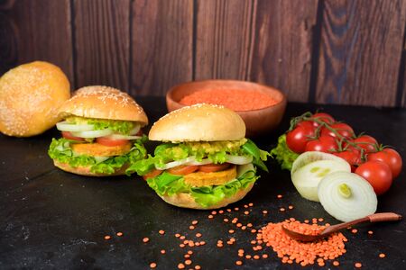 vegetarian hamburger with lentil cutlet, avocado, tomatoes, onions, lettuce on a wooden table on a dark background. delicious Burger for vegetarians.の写真素材