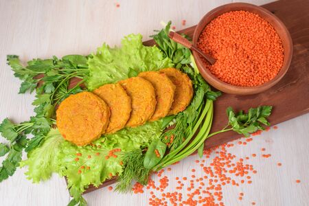 vegetarian cutlets from lentils and carrots in a wooden plate with vegetables and herbs. healthy food. red lentils in a wooden plate on a light background. the view from the top. close upの写真素材