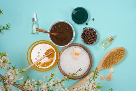 Spa products for home body care for cellulite and acne. sea salt, coffee scrub, honey in plates on a blue background and a flower branch. spring composition of organic ingredients.の写真素材