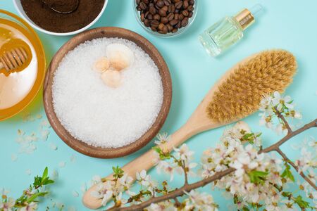 Spa products for home body care for cellulite and acne. sea salt, coffee scrub, honey in plates on a blue background and a flower branch. spring composition of organic ingredients.の写真素材