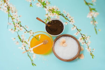 Spa products for home body care for cellulite and acne. sea salt, coffee scrub, honey in plates on a blue background and a flower branch. spring composition of organic ingredients.の写真素材