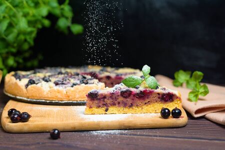 pie with black currant and shortbread, fresh berries. the pie is cut into pieces and the top is sprinkled with powdered sugar . close-up of a piece in the pie section.の写真素材