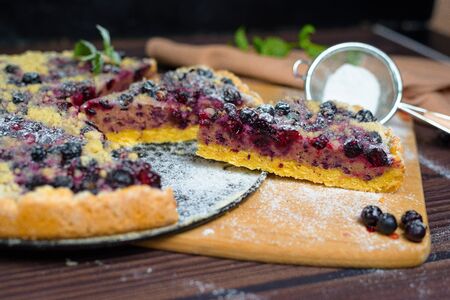 pie with black currant and shortbread, fresh berries. the pie is cut into pieces and the top is sprinkled with powdered sugar . close-up of a piece in the pie section.の写真素材