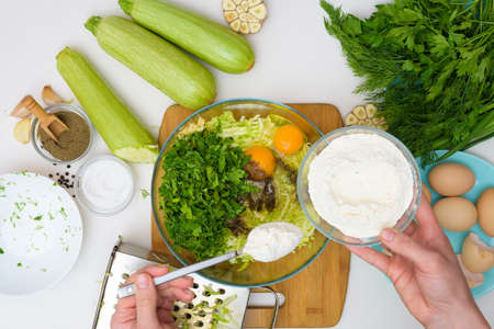 step-by-step recipe to cook pancakes of zucchini and greens on a light background. with the addition of eggs, flour, garlic, pepper. add the flour to the zucchini. the view from the top.の写真素材