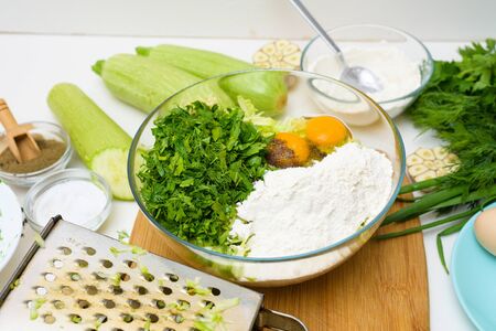 step-by-step recipe to cook pancakes of zucchini and greens on a light background. with the addition of eggs, flour, garlic, pepper. pour the chopped whole to the zucchini. the view from the top.の写真素材