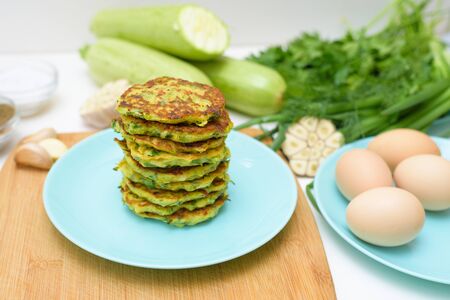 veggie fried pancakes with zucchini and greens on a blue plate on a light background on a wooden Board . recipe with the addition of eggs and flour. top view, selective focus, space for text.の写真素材