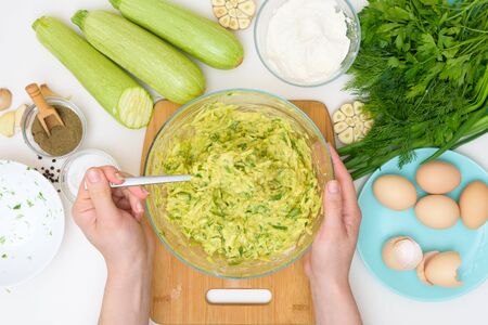 step-by-step recipe to cook pancakes of zucchini and greens on a light background. with the addition of eggs, flour, garlic, pepper. mix the ingredients in a bowl. the view from the top.の写真素材
