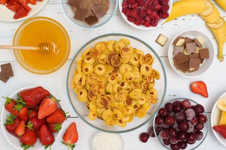 mini pancake cereal bowl with fresh strawberries banana chocolate, coconut shavings and honey in small plates. the view from the top . the trend of self-isolation.の写真素材