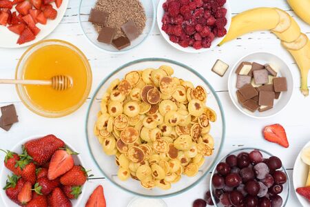 mini pancake cereal bowl with fresh strawberries banana chocolate, coconut shavings and honey in small plates. the view from the top . the trend of self-isolation.の写真素材