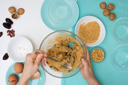 ingredients for the recipe homemade oatmeal cookies with dates, peanuts, coconut chips in glass plates on a light background. the view from the top, mixing with your hands ingredients.の写真素材