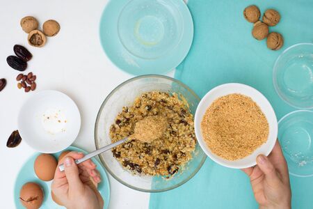 ingredients for the recipe homemade oatmeal cookies with dates, peanuts, coconut chips in glass plates on a light background. the view from the top, mixing with your hands ingredients.の写真素材