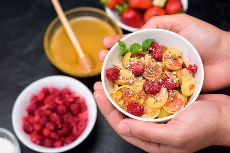 mini pancake cereal bowl with fresh strawberries banana chocolate, coconut shavings and honey in small plates. the view from the top . the trend of self-isolation.の写真素材
