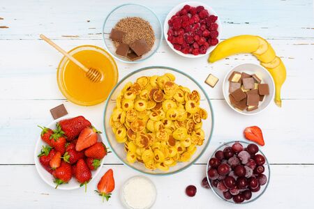 tiny pancake cereal bowl with fresh strawberries banana chocolate, coconut shavings and honey in small plates. the view from the top . the trend of self-isolation.の写真素材