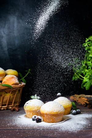 cupcakes with mint and blackcurrant leaves in powdered sugar on a black background, a wooden basket with cupcakes and blackcurrants . levitation of powdered sugar on muffins.の写真素材