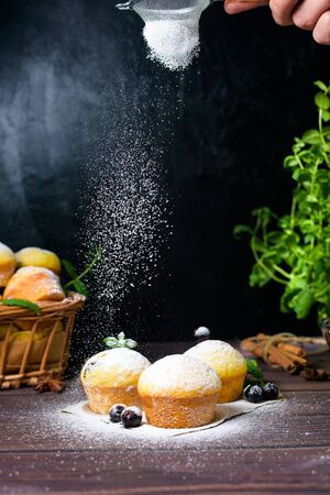 cupcakes with mint and blackcurrant leaves in powdered sugar on a black background, a wooden basket with cupcakes and blackcurrants . levitation of powdered sugar on muffins.の写真素材
