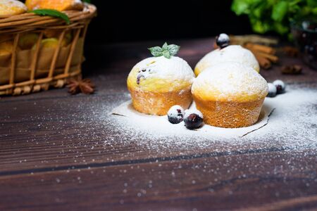 cupcakes with mint and blackcurrant leaves in powdered sugar on a black background, a wooden basket with cupcakes and blackcurrants . close-up, space for text.の写真素材