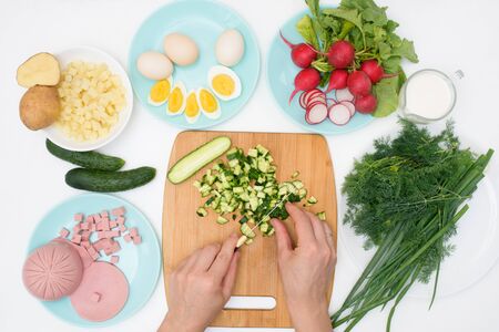 step by step recipe for Russian cold okroshka soup, ingredients for homemade okroshka cut with a knife-sausage, herbs, eggs, cucumbers, potatoes, radishes. top view on a light background.の写真素材