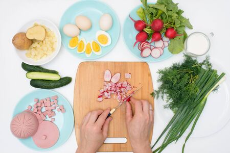 step by step recipe for Russian cold okroshka soup, ingredients for homemade okroshka cut with a knife-sausage, herbs, eggs, cucumbers, potatoes, radishes. top view on a light background.の写真素材