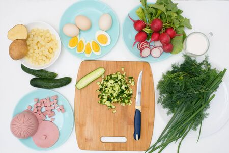 step by step recipe for Russian cold okroshka soup, ingredients for homemade okroshka cut with a knife-sausage, herbs, eggs, cucumbers, potatoes, radishes. top view on a light background.の写真素材