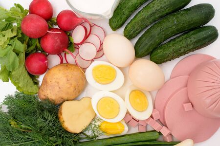 ingredients for a recipe of homemade Russian national cold okroshka soup on a light background. potatoes, radishes, sausage, onions, herbs, eggs. top view close-up.の写真素材