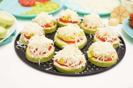 step by step recipe and ingredients for cooking homemade zucchini mini portioned pizza with mozzarella and tomatoes, pepper and garlic. top view on a light backgroundの写真素材