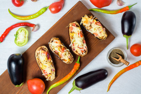 preparation homemade stuffed eggplant in the shape of a boat with baked vegetables and mozzarella cheese, ingredients tomatoes, peppers, onions, eggplant. on a light background top view.の写真素材