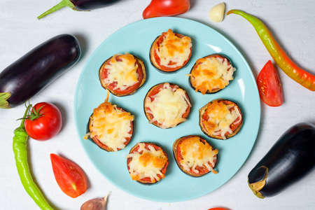 cooking homemade vegan pizza eggplant bites, tomatoes, peppers, mozzarella on a blue plate. eggplant stacked on a light background.の写真素材