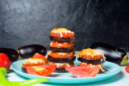 cooking homemade vegan pizza eggplant bites, tomatoes, peppers, mozzarella on a blue plate. eggplant stacked on a dark background.の写真素材