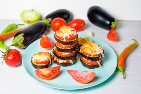 cooking homemade vegan pizza with eggplant on a bite, tomatoes, peppers, mozzarella on a blue plate. eggplant piled up on a light background.の写真素材