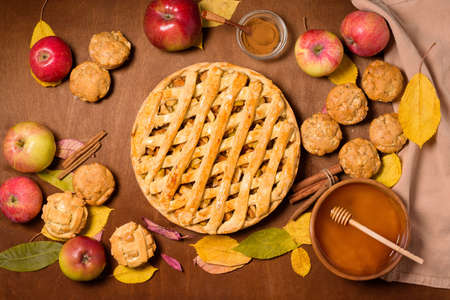 autumn baking concept with seasonal apples and cinnamon. Apple pie, crumble, crisp, and muffins, cupcakes. top view on a wooden background with autumn yellow leavesの写真素材