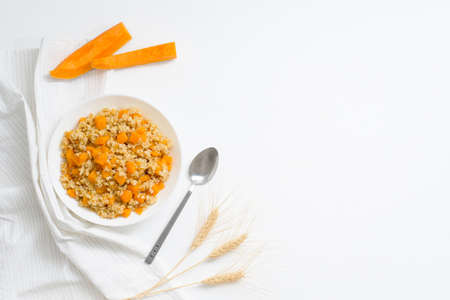 homemade oatmeal porridge with seasonal autumn pumpkin in a white plate on a light background top view. autumn composition with wheat ears and pumpkin, ingredients for porridge.の写真素材