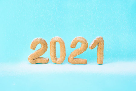 number 2021 of ginger cookies is sprinkled with powdered sugar on a blue background. festive new...