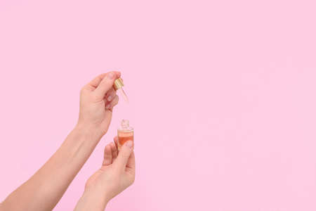 Cosmetic serum in transparent glass dropper bottles on a pink background in a woman's hand. the concept of natural skin care products. Essence skin care products for beautiful healthy skin.の写真素材