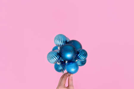 a woman's hand holds Christmas tree balls white and blue on a pink background. concept 2021, minimalism, copy space mockup for postcards.の写真素材
