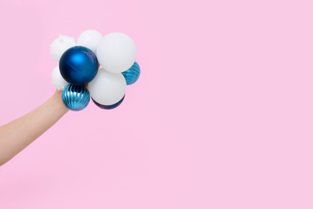 a woman's hand holds Christmas tree balls white and blue on a pink background. concept 2021, minimalism, copy space mockup for postcards.の写真素材