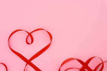 valentine's day red ribbon curves in the shape of a heart on a pink background. festive background for wedding and greeting cards, mockup, copy space.の写真素材