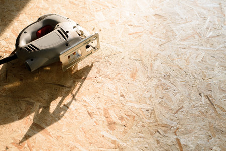 the process of sawing plywood with an electric jigsaw, a man holds a tool in his hand