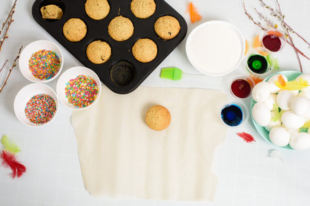 the process of decorating mini cupcakes Easter cakes with white icing and sweet candies, top view, willow branches and eggs for coloring.の写真素材