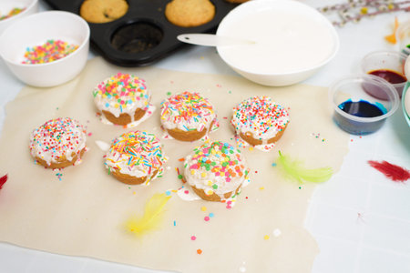 the process of decorating mini cupcakes Easter cakes with white icing and sweet candies, top view,...